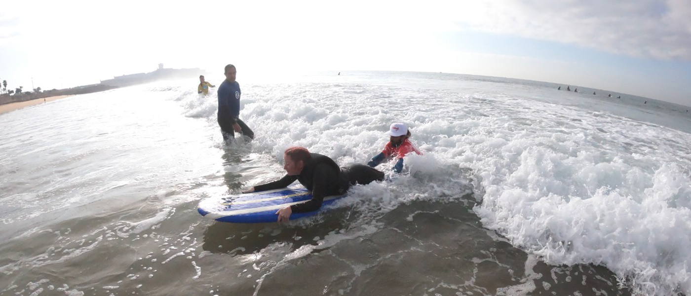 Football For All Leadership Programme participant at an adapted surf session, on a surf board with a volunteer supporting her