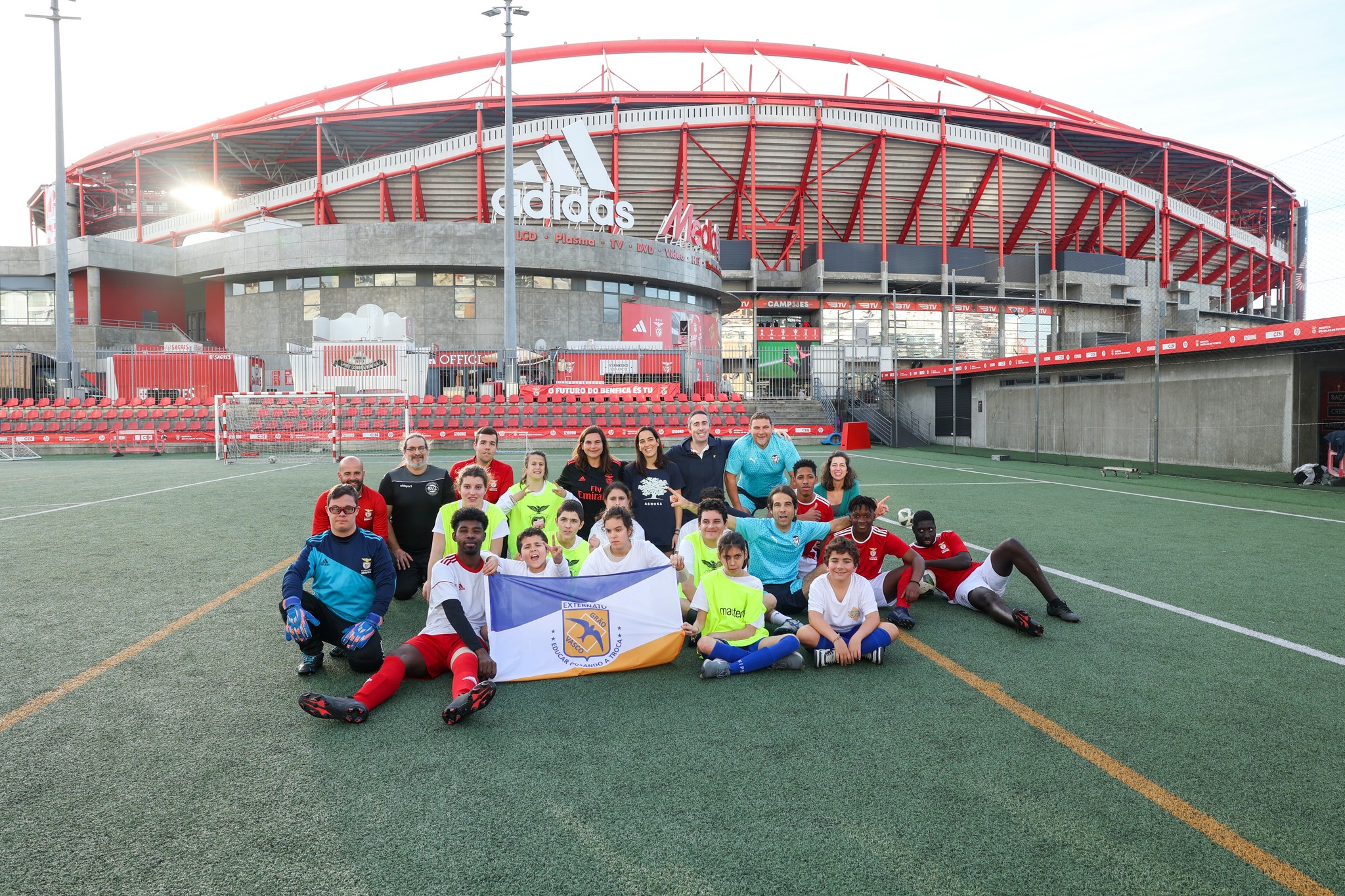 Group of participants in the intellectual disabilities football workshop and project team pictured on a training pitch, featuring the Benfica Stadium in the background