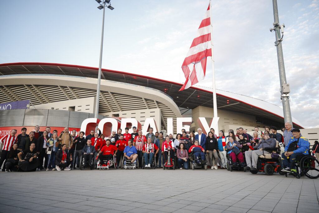 Group of people with disabilities gathered in front of the flag at the Metropolitano stadium of Atlético de Madrid.