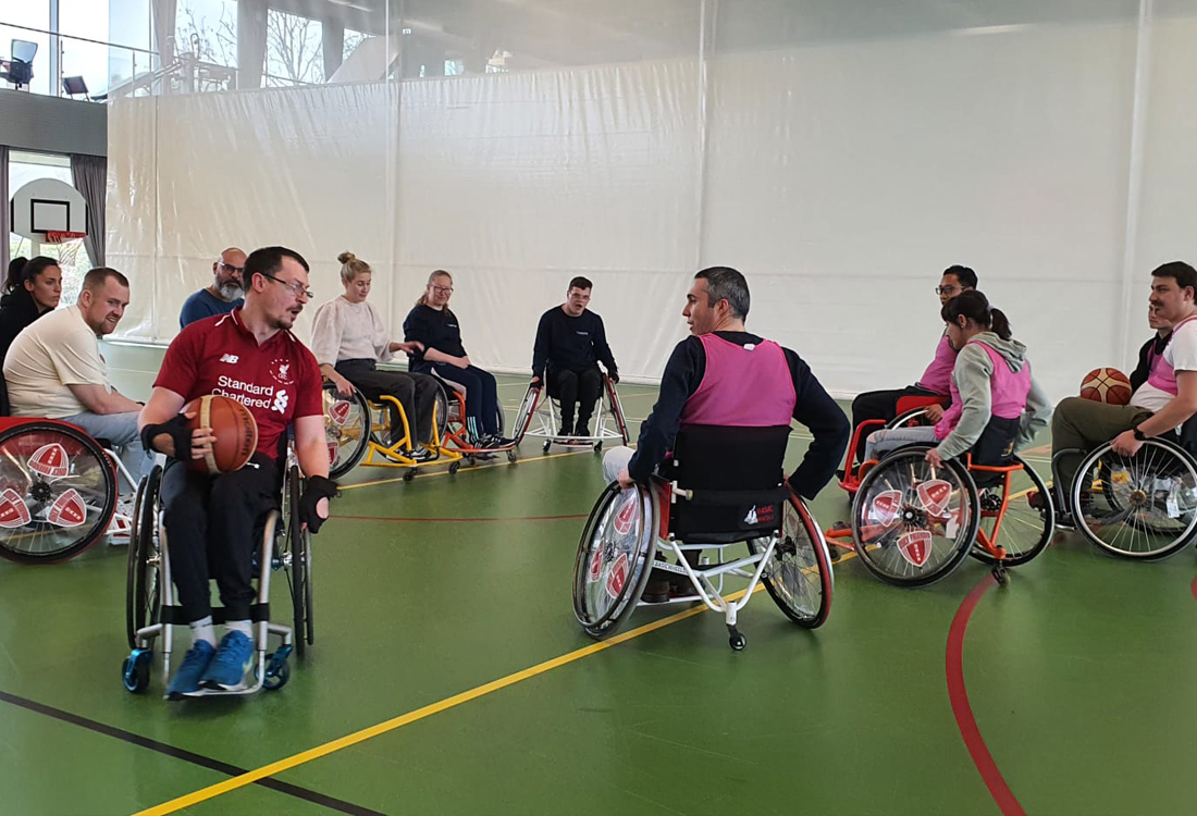 2 powerchair football players challenging the ball with their backs to the camera, one is in a red jersey and the other in a green jersey